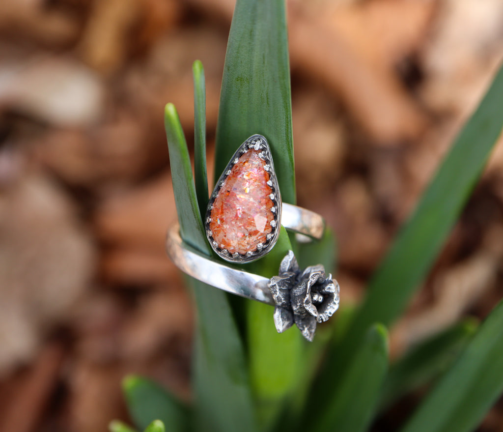 A closer photo of the sunstone ring with the daffodil places on a cluster of real daffodil leaves.