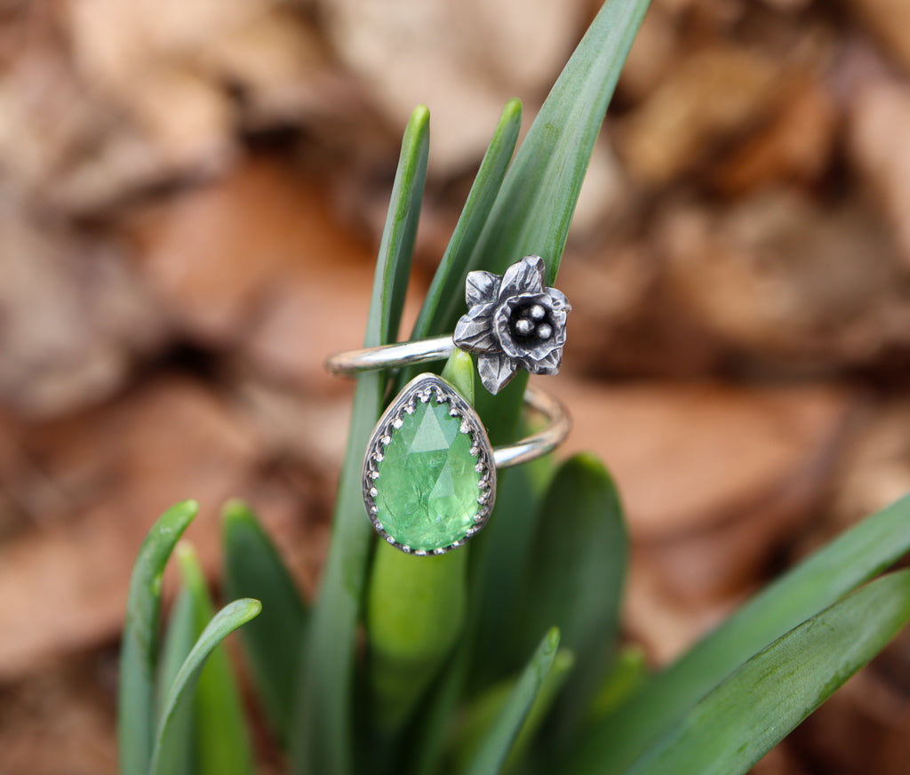 A close up photo of the green tsavorite garnet stone on a cluster of daffodil leaves.
