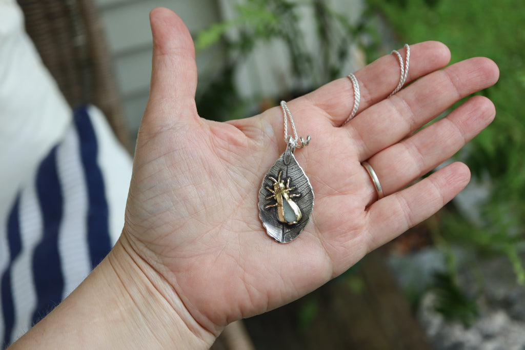 A hand is shown holding the firefly necklace to show size. It is about 2 inches tall total.