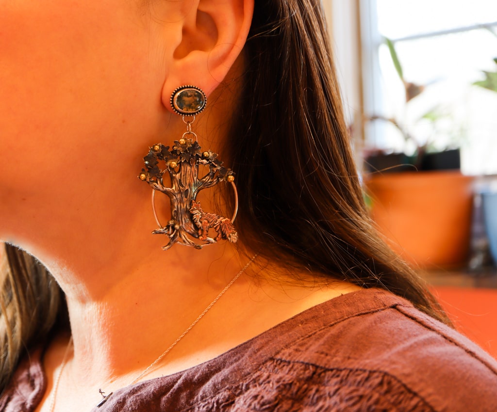 the fox and apple tree earrings are being shown worn on a woman with long dark hair and a dark purple shirt.