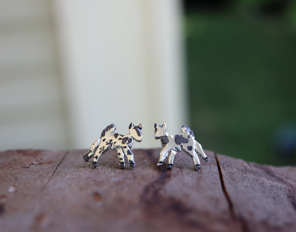 A closer look at the sterling silver baby goat earrings shown on a piece of dark brown wood.