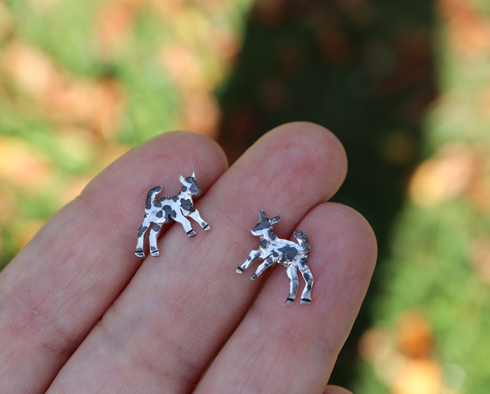A hand is shown holing the small sterling silver goat stud earrings for size reference. They are about 1/2 inch wide.
