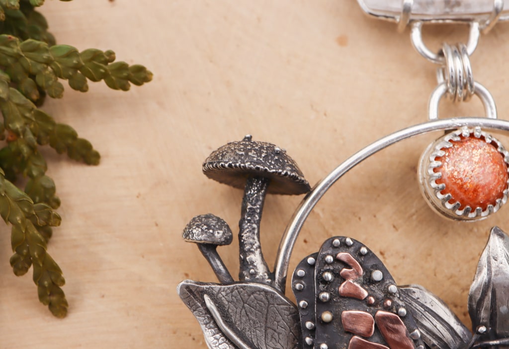 A close up of the two tiny silver mushrooms to the left of the monarch butterfly. You can also see the bright orange round sunstone.