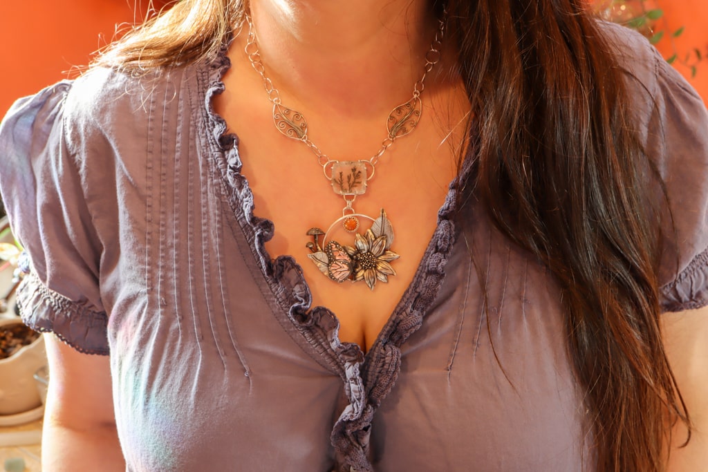 The necklace is shown being worn by a woman with medium brown hair and a light purple shirt.