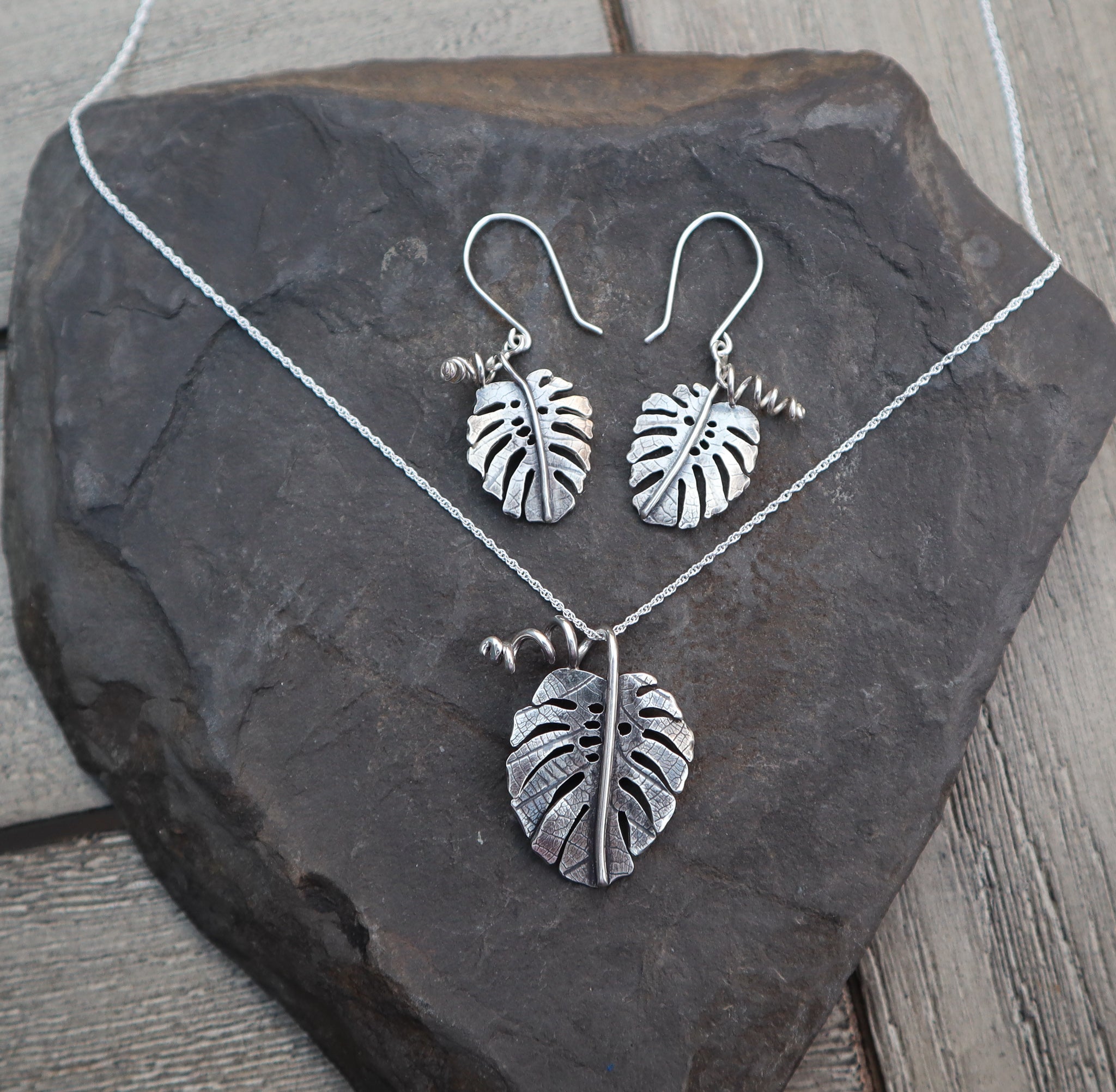 A monstera deliciosa earring and necklace set shown on a piece of dark grey slate stone.
