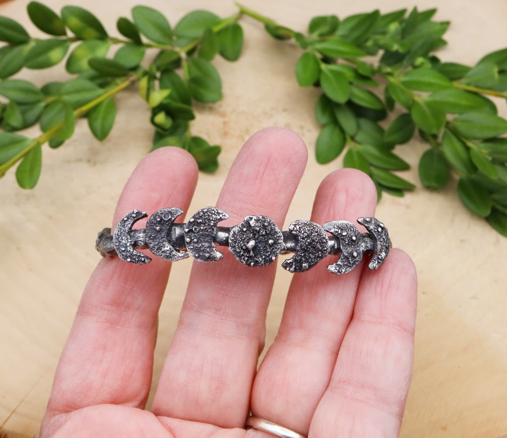 A hand is shown holding the bracelet for size reference. The moons are each about 1/2 inch tall and hand cut.