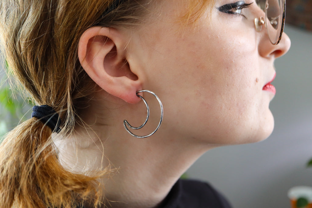 Sterling silver moon earring hoops being worn on a woman model to show their size. They are about 1.5 inches tall and are stud earrings.
