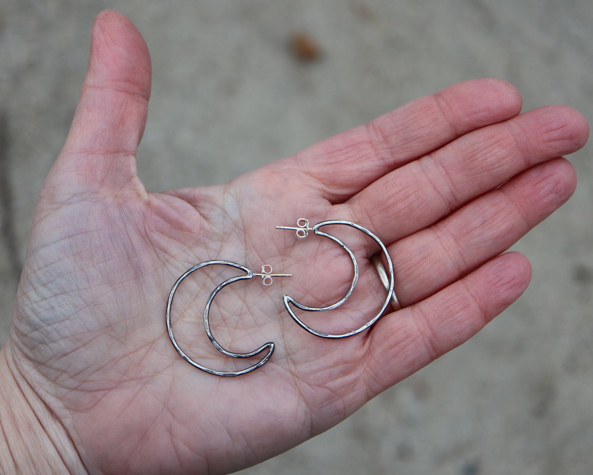 A hand is shown holding the sterling silver crescent moon hoops earrings to show size. They are about 1.25 inches tall.