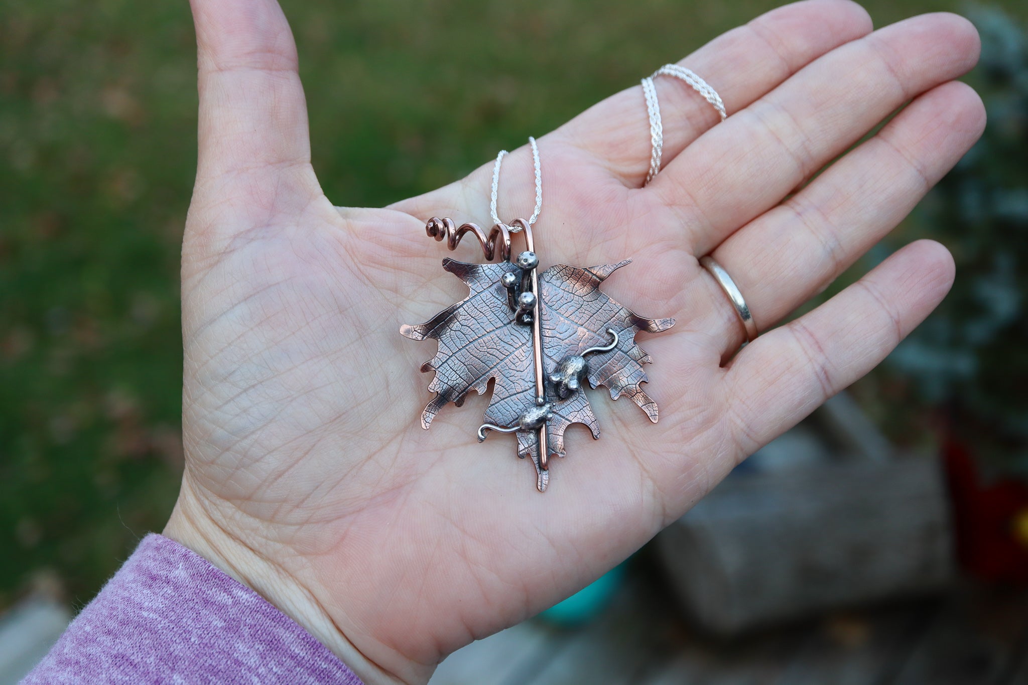 A hand is shown holding the copper maple leaf necklace to show it's size.