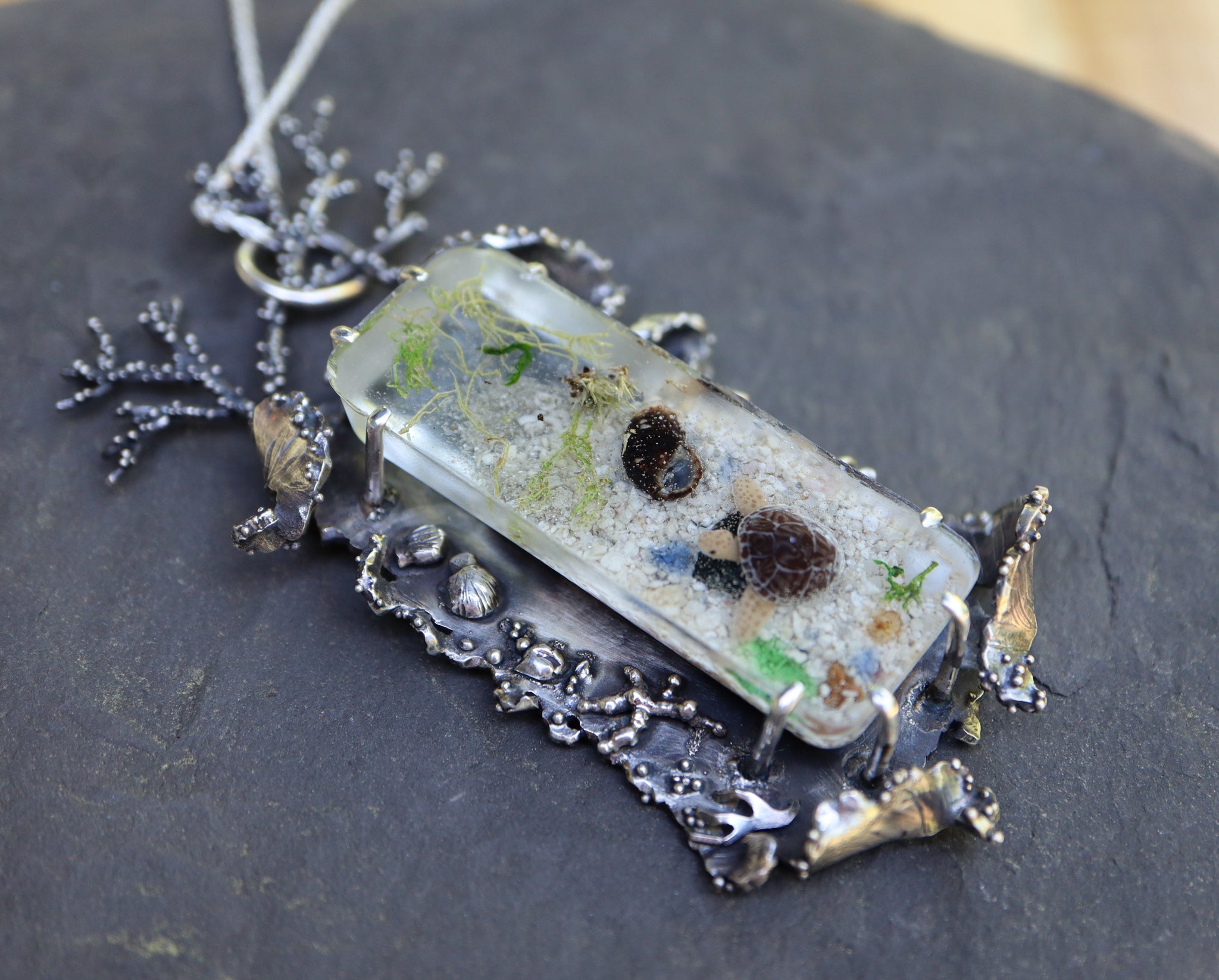 A side view of the pendant showing the hand carved silver sea shells, seaweed, and waves along the left side of the pendant.