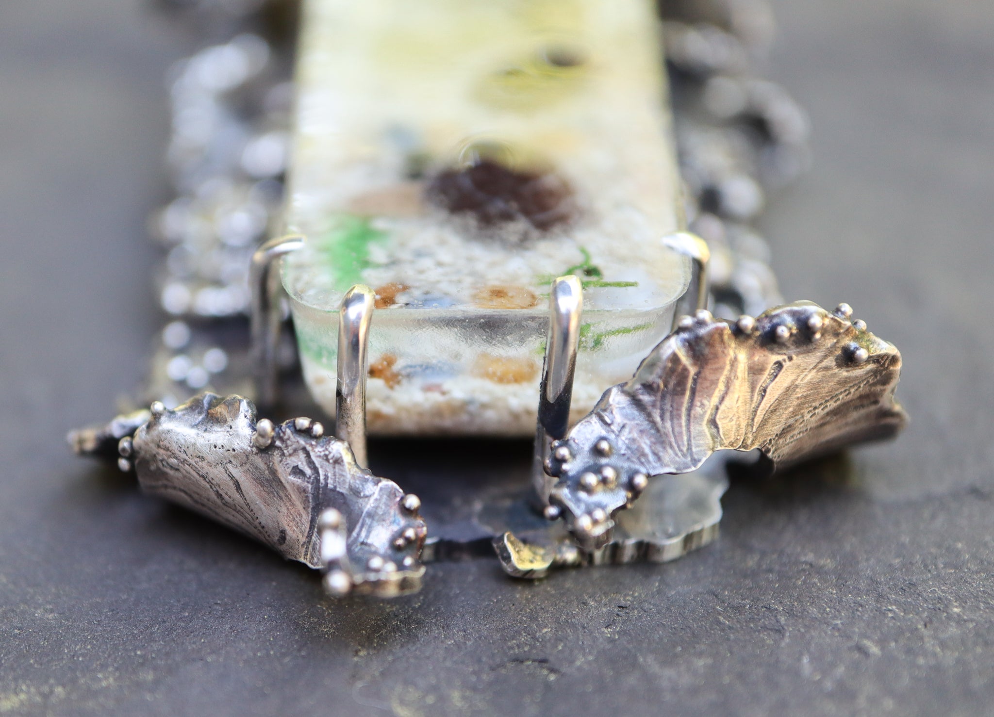 The bottom of the pendant showing the lapping waves that are curled up around the resin cabochon.