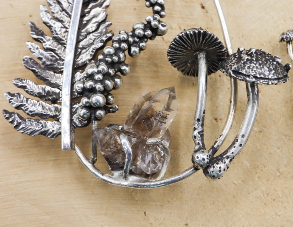 A close up of the other earring featuring a cluster of Herkimer diamond quartz points. There is a fern on one side and mushrooms on the other side.