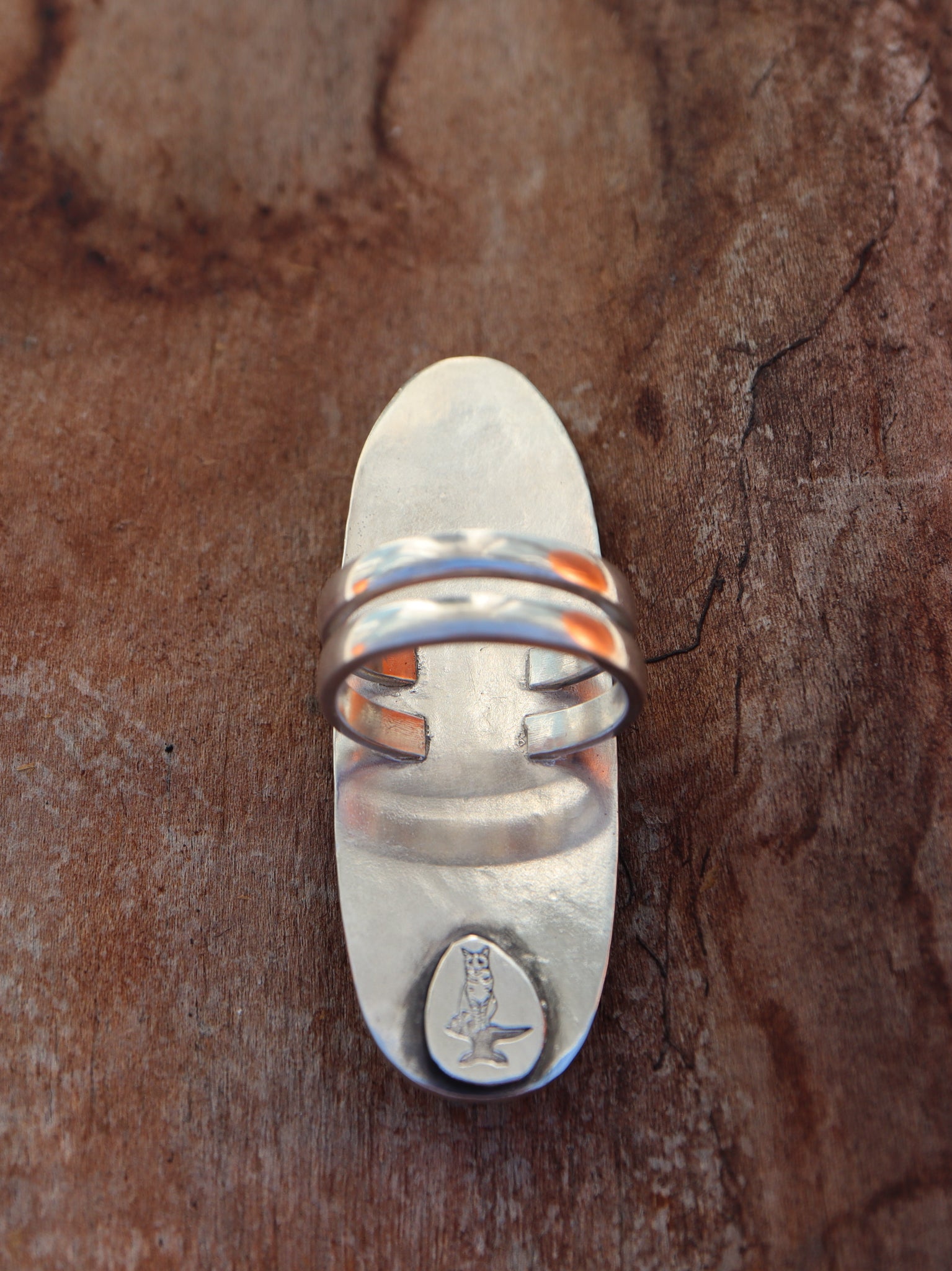 The back of the ring with a double band. The ring is shown on a piece of dark brown wood.