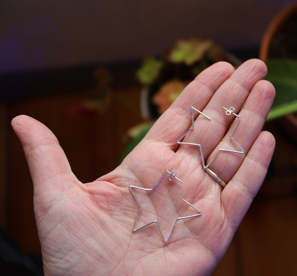 A hand is shown holding a pair of sterling silver star shaped hoop earrings.
