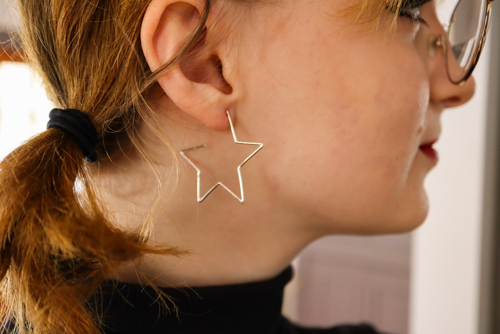 A young women with blonde hair is shown wearing a pair of sterling silver star shaped hoop earrings.