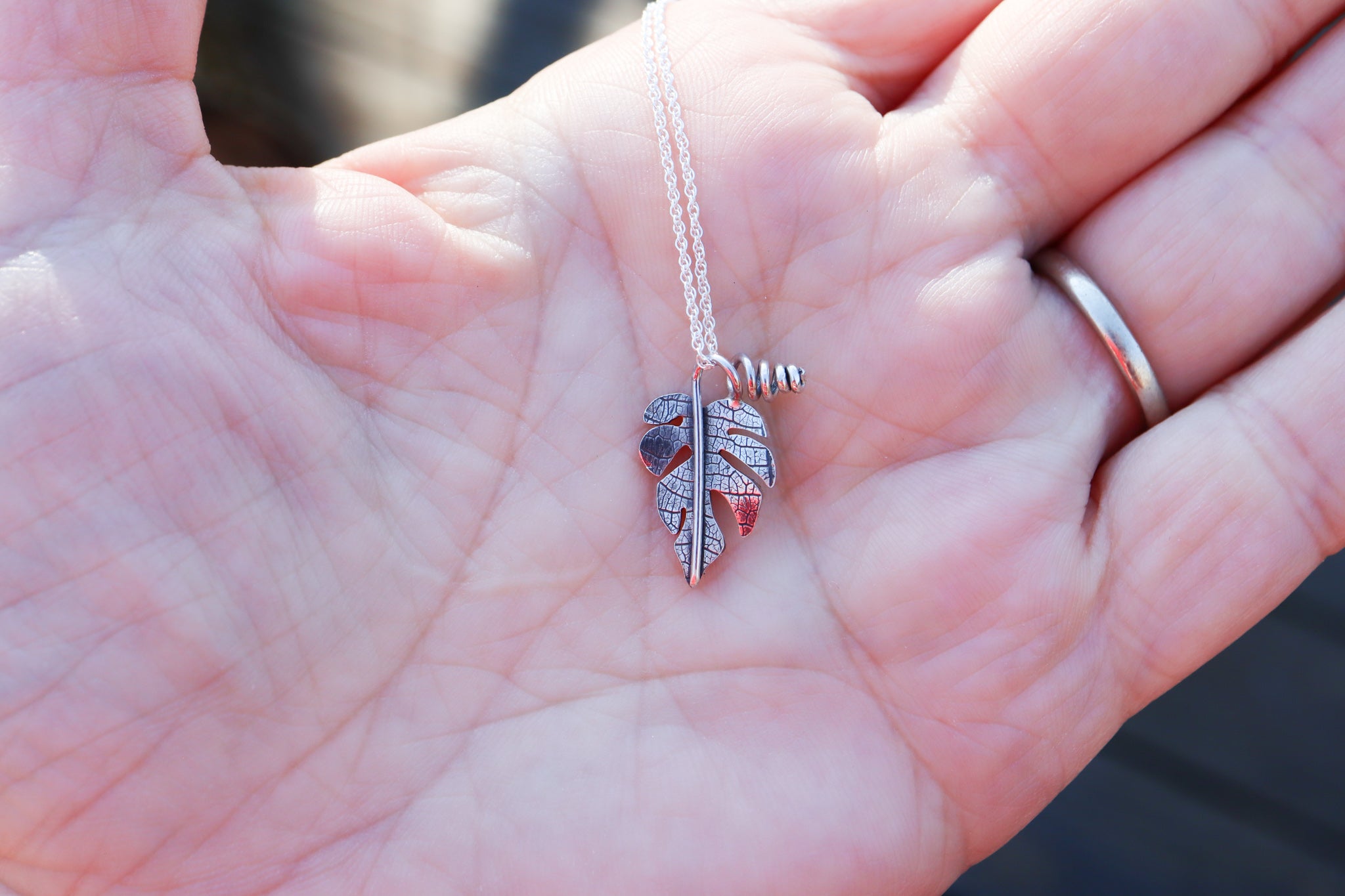 A small sterling silver handmade rhaphidophora tetrasperma necklace being shown held in a hand to show size scale.