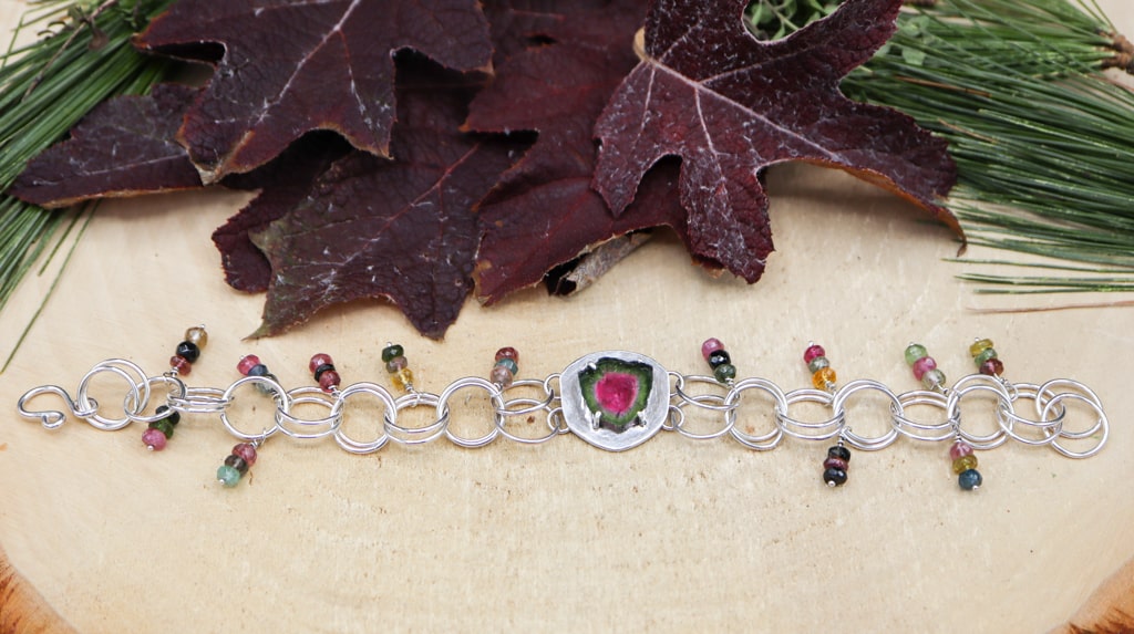 This is the bracelet outstretched showing all of the colors. There are dark red leaves and pine needles above the bracelet.