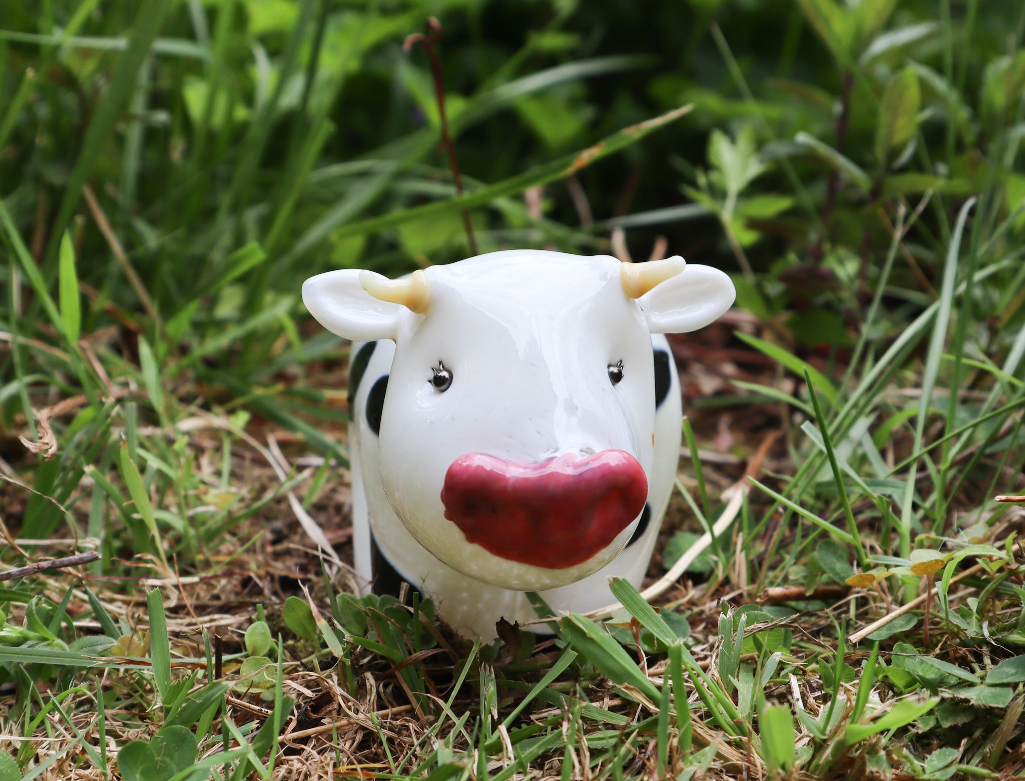 Handmade glass Holstein cow sitting in the grass.