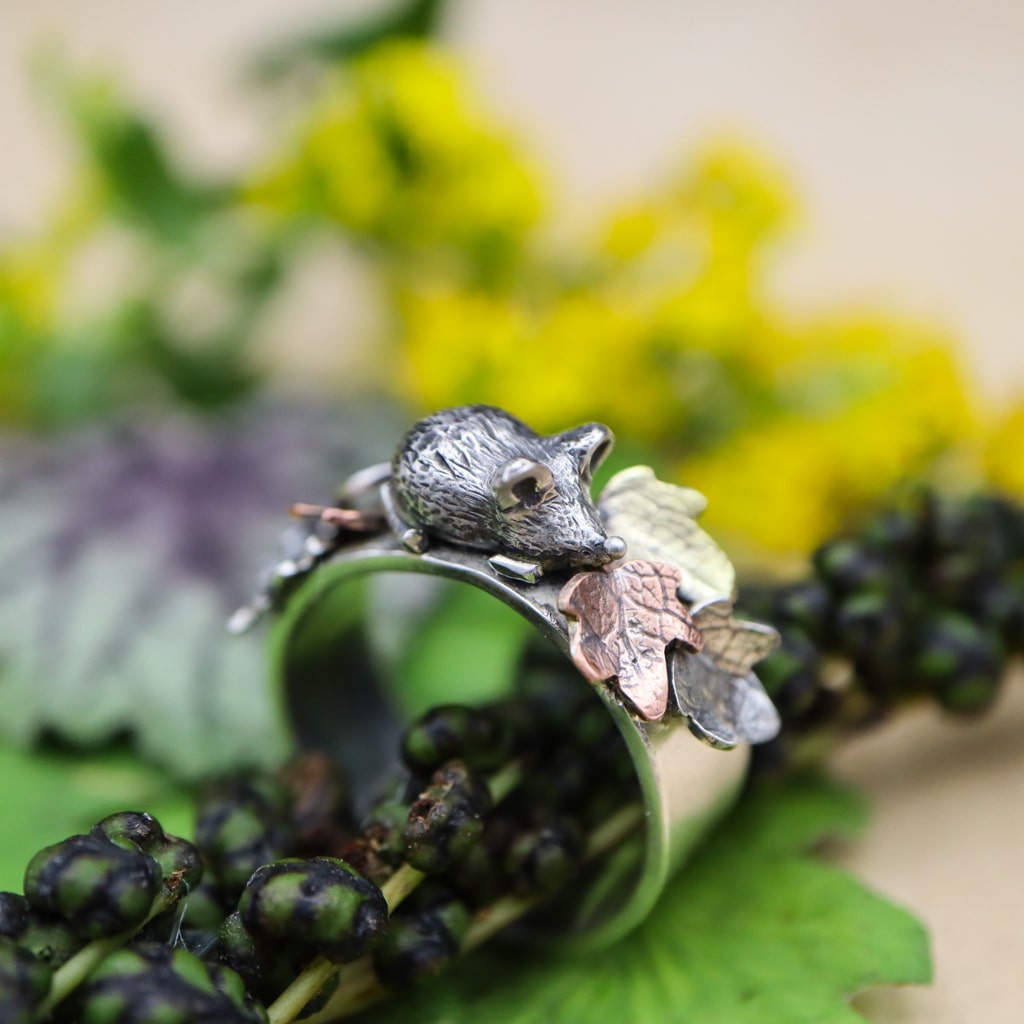 A sterling silver ring featuring a tiny hand carved mouse in the center of copper, brass, and silver fall leaves. this is the side view of the mouse and the leaves.