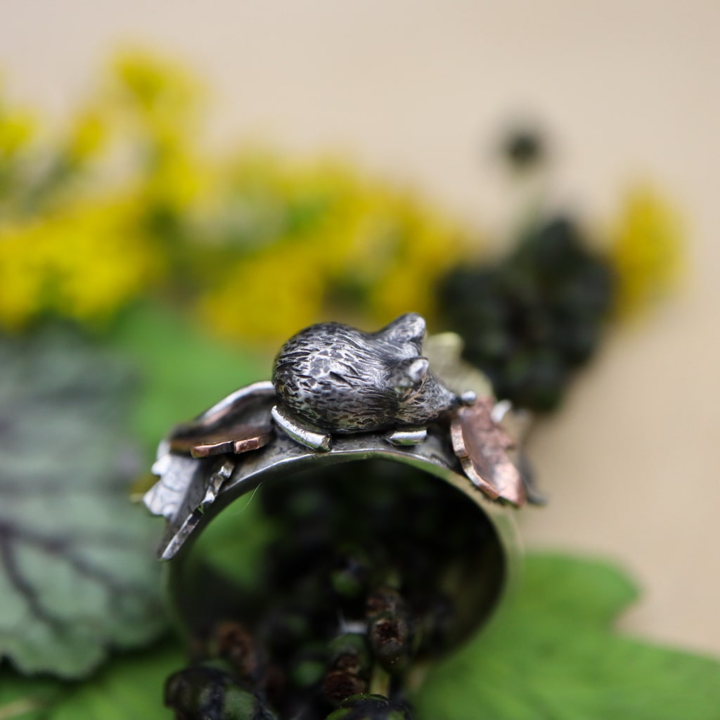 A sterling silver ring featuring a tiny hand carved mouse in the center of copper, brass, and silver fall leaves. this is the side of the fluffy looking mouse.