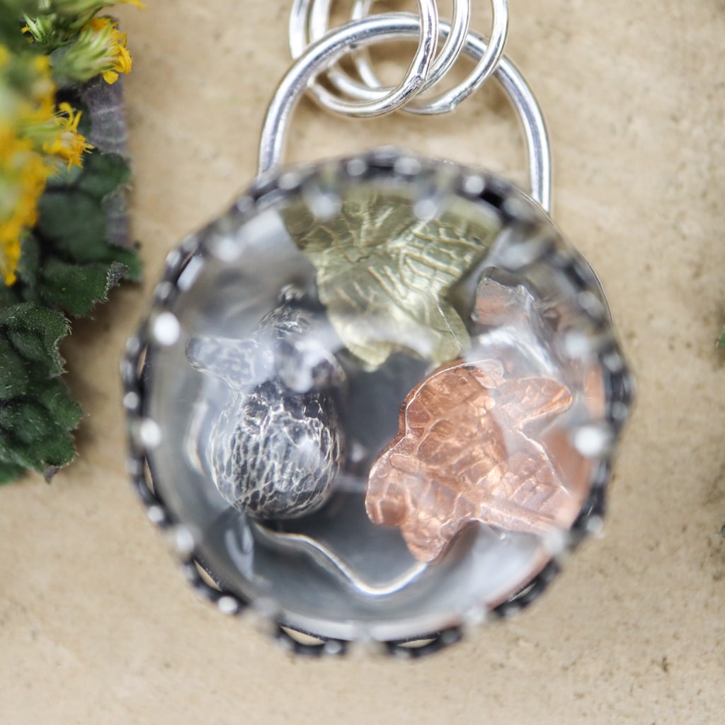 A very close up photo of the inside of the pendant showing the little mouse and the three fall leaves.