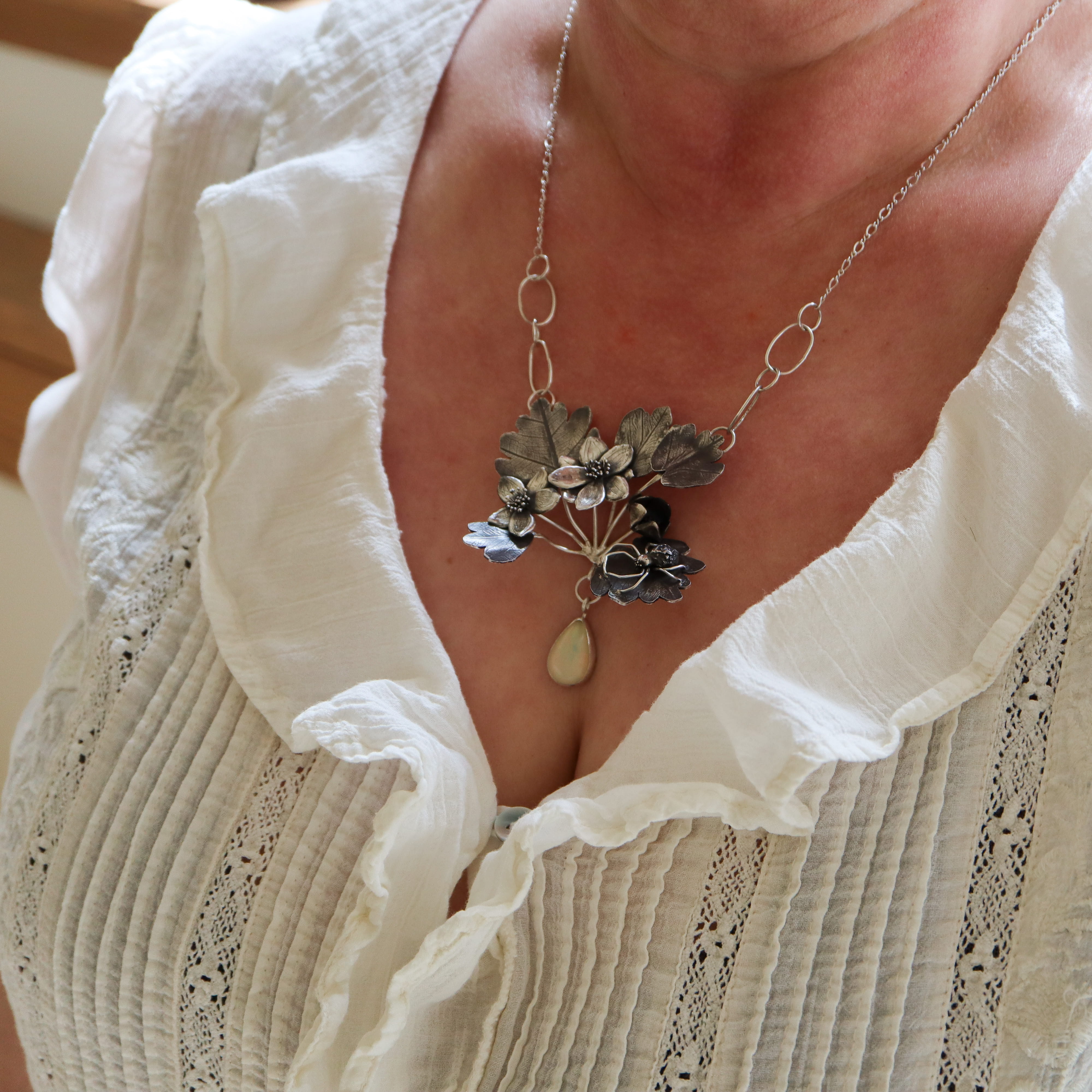 A woman in a white blouse is shown wearing the crab spider and rue anemone necklace with opal. 