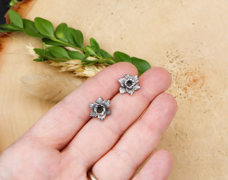 A hand is shown holding the sterling silver daffodil flower stud earrings to show their size. 