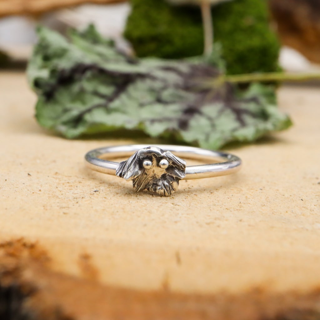 Sterling silver handmade tiny ghost ring. He is shown on a plain silver band and pictured on a light tan piece of wood. 