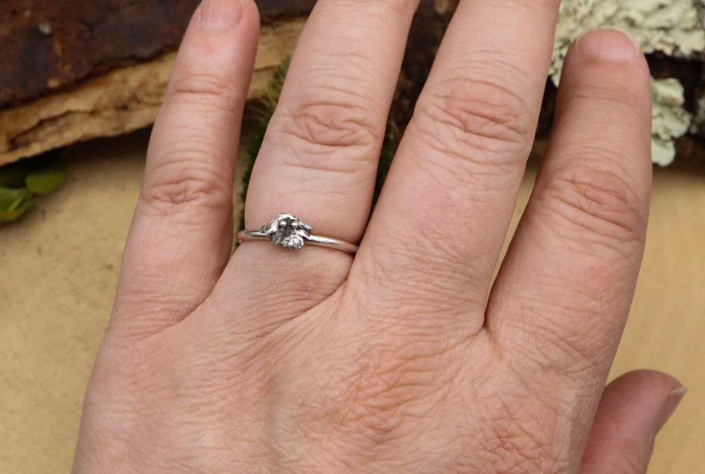 A hand is shown wearing the tiny silver ghost ring. 