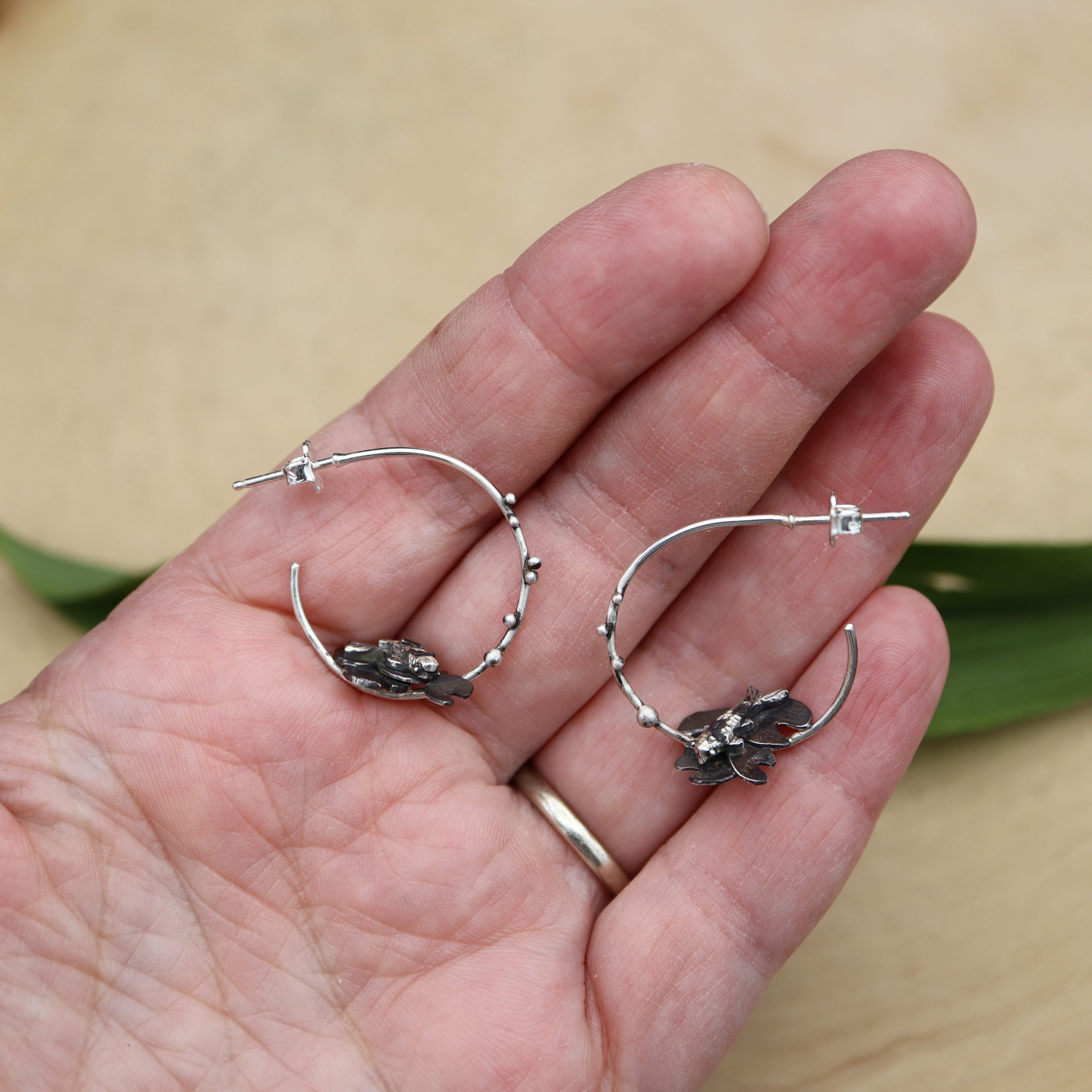 A hand is shown holding the sterling silver fish hoop earrings for size reference. 