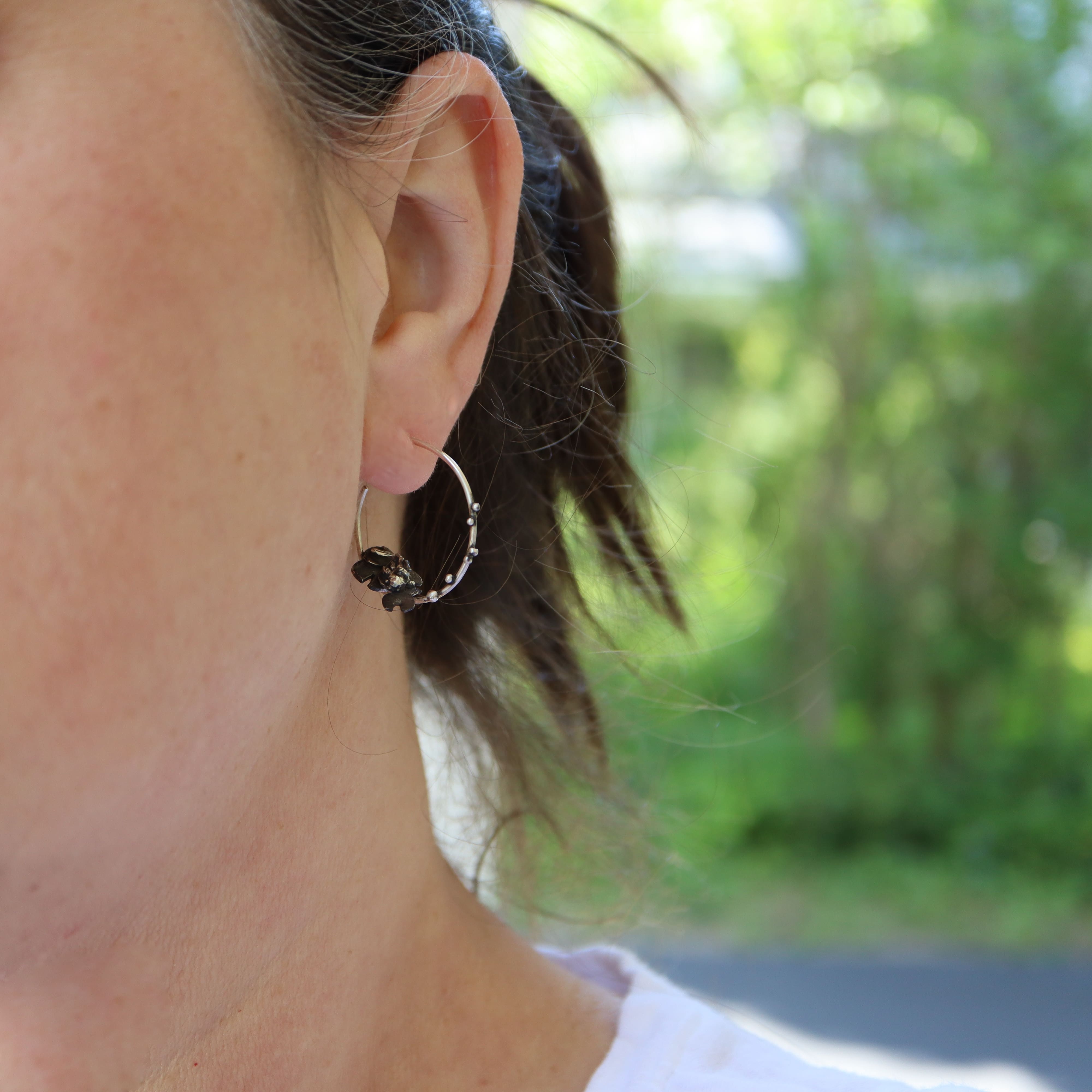Close-up of an ear wearing a goldfish hoop earring with a blurred natural background