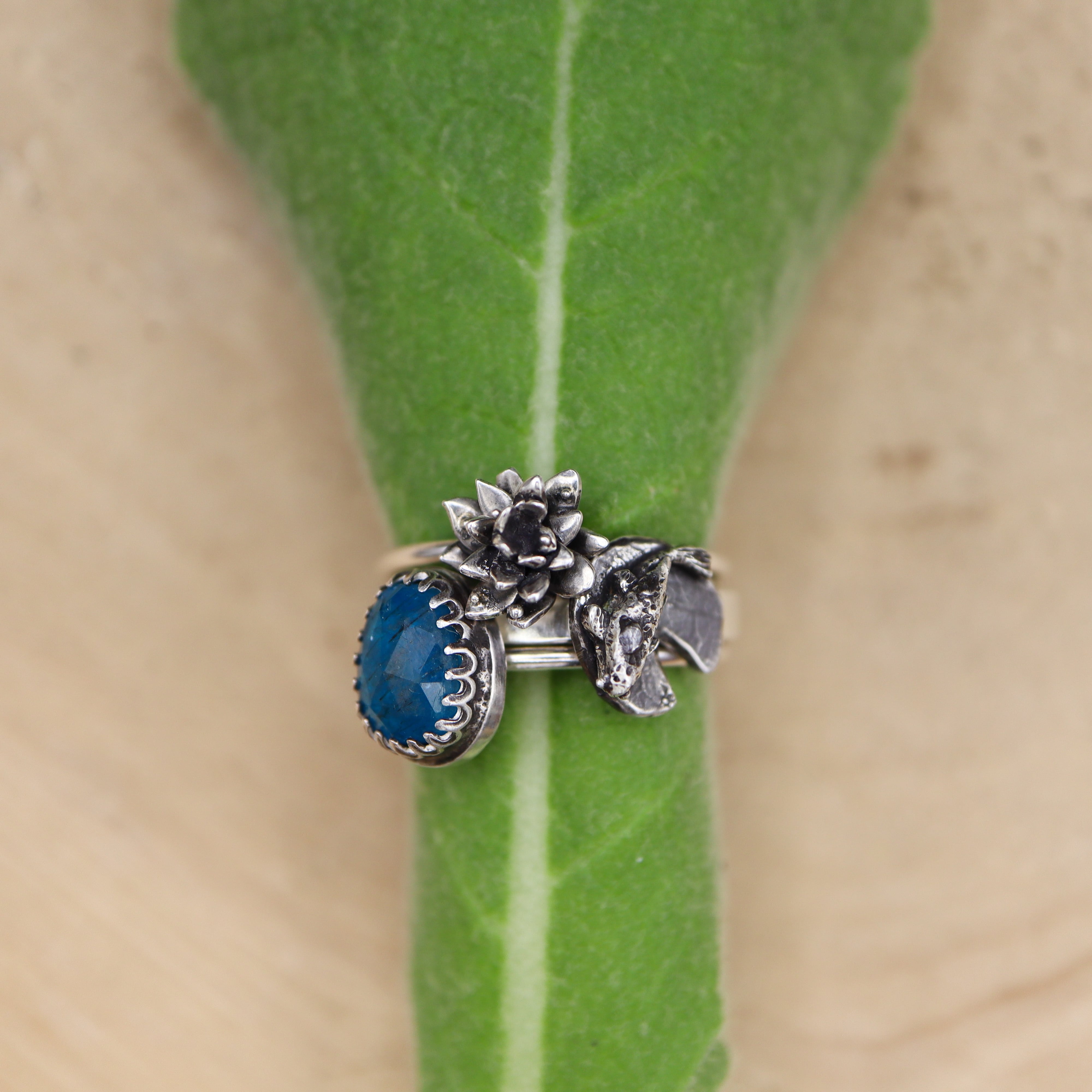 A set of three sterling silver handmade rings featuring a blue apatite gemstone, a water lily flower, and a hand carved goldfish on a lily pad. 