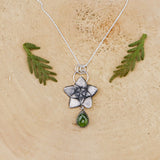 Hoya flower bud necklace is shown on a light tan piece of wood. The flower is about 1 inch tall and below it is a dark green pear shaped vesuvianite stone.