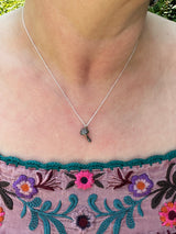 The dainty mushroom necklace is shown being worn by someone with a light pink floral embroidered shirt. 