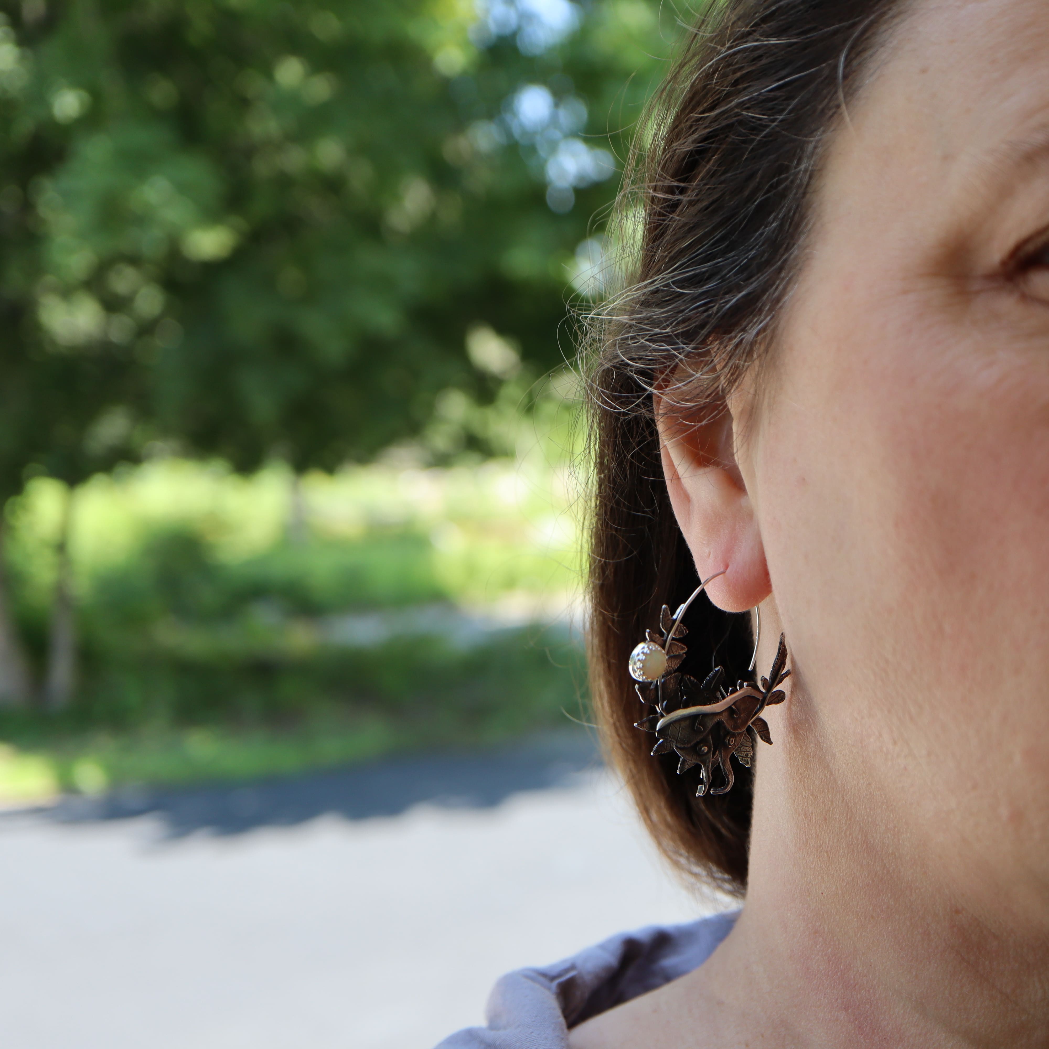 Close-up of a person wearing a luna moth earring with a blurred natural background