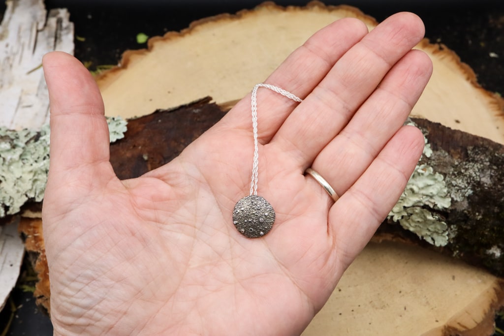 A hand is shown holding the sterling silver full moon necklace. 