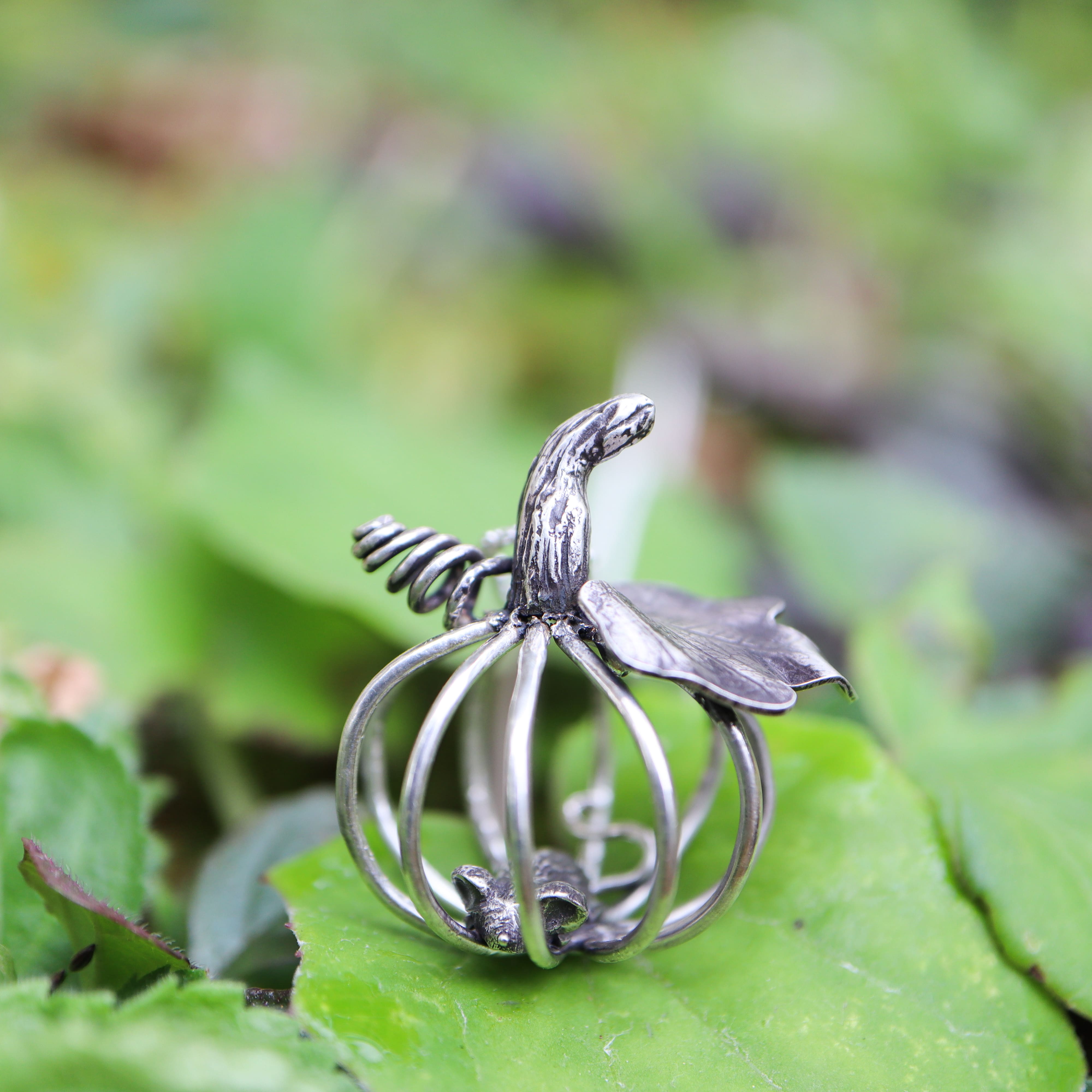Silver necklace shaped like a pumpkin with a leaf on a green leaf background and a silver mouse inside the pumpkin
