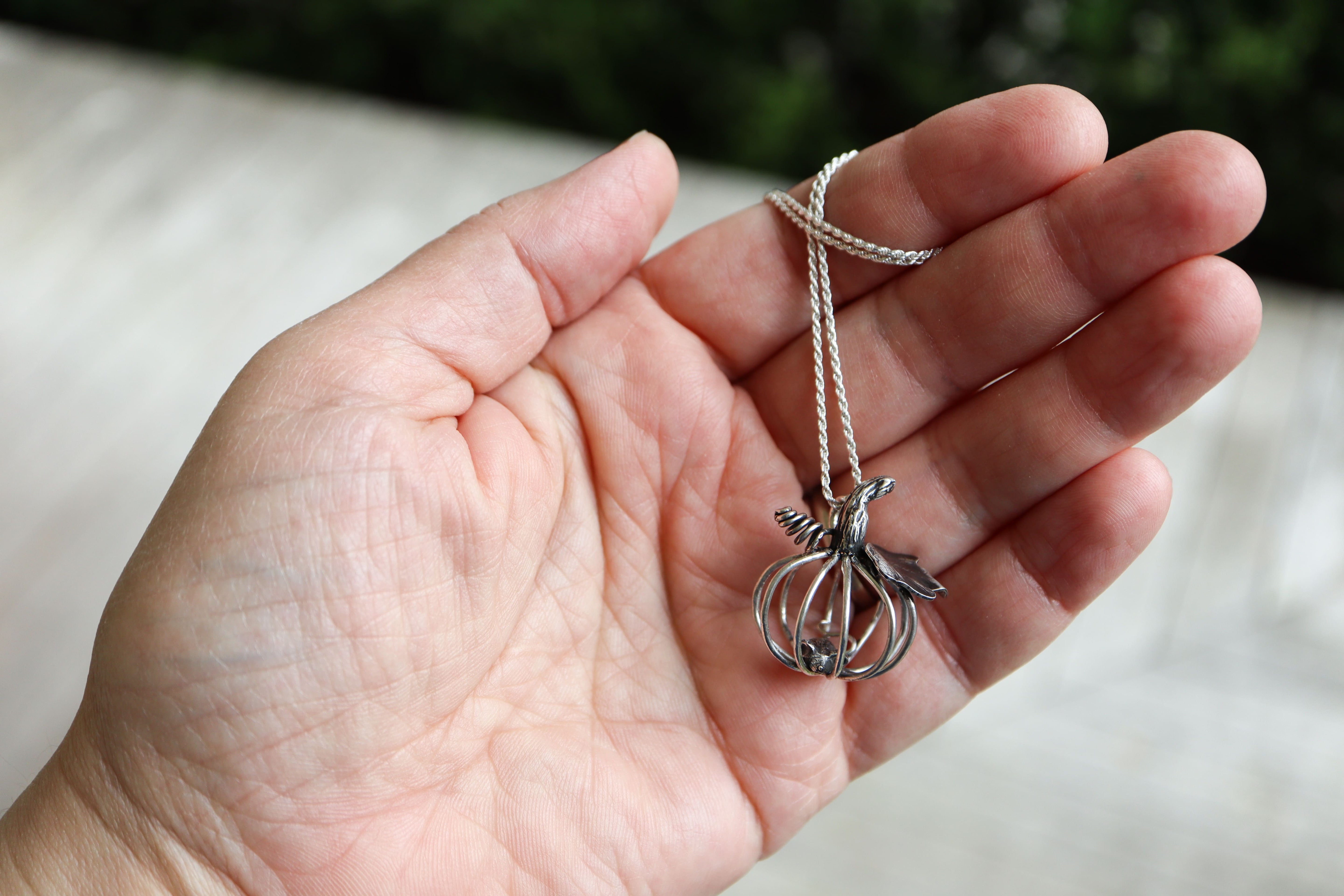 Hand holding a silver pumpkin and mouse necklace against a blurred background