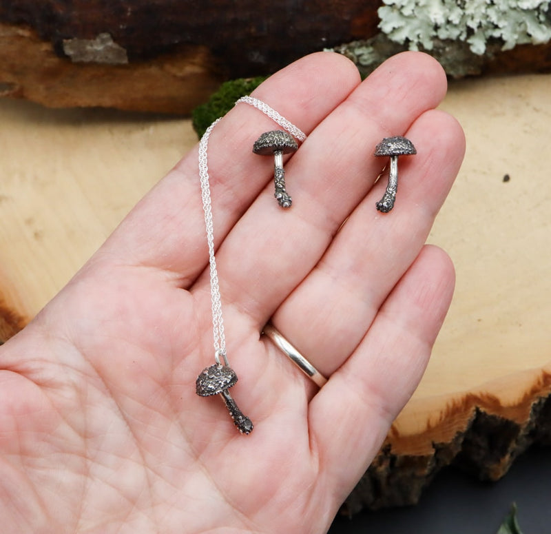 A hand is shown holding the mushroom earrings and necklace set to show size. Each of them is only about .75 inches tall. 