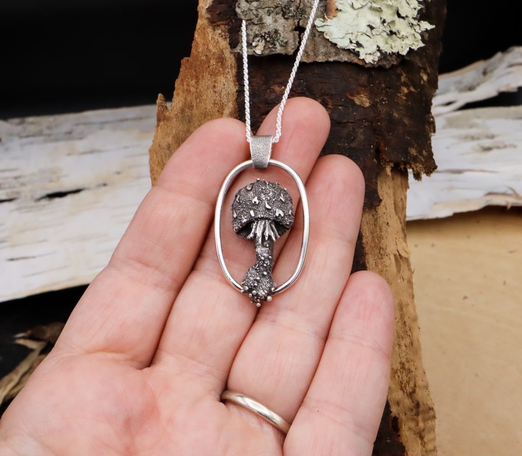 A hand is shown holding the mushroom necklace for size reference. It is about 2 inches tall. 