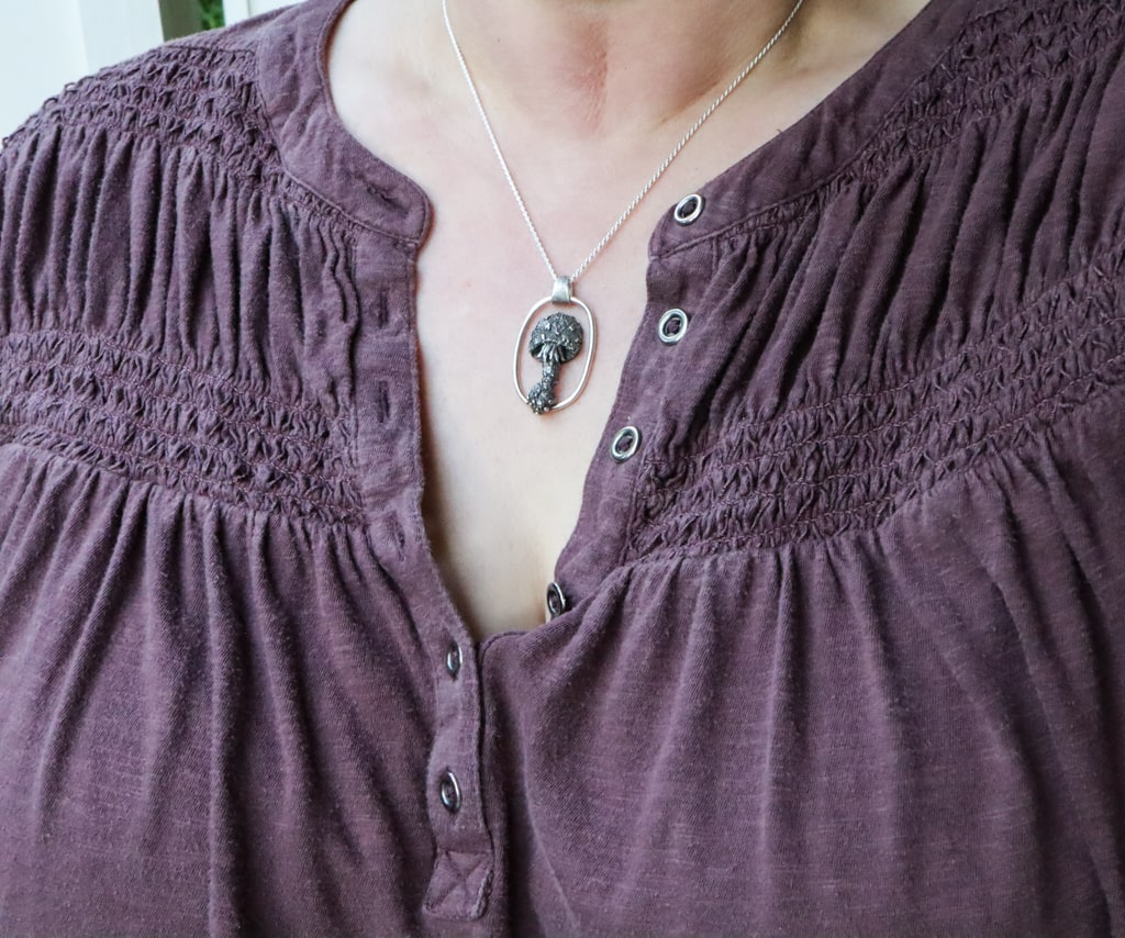 The necklace is shown being worn on someone with a dark purple ruffled shirt. 