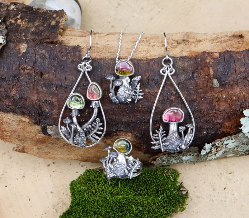 A set of earrings and ring are shown together with the watermelon tourmaline necklace. They are grouped together on a piece of dark brown wood. 