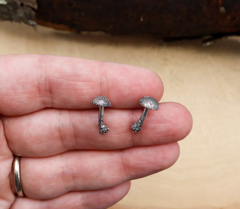 A hand is shown holding the 1/2 inch tall sterling silver mushroom stud earrings. 