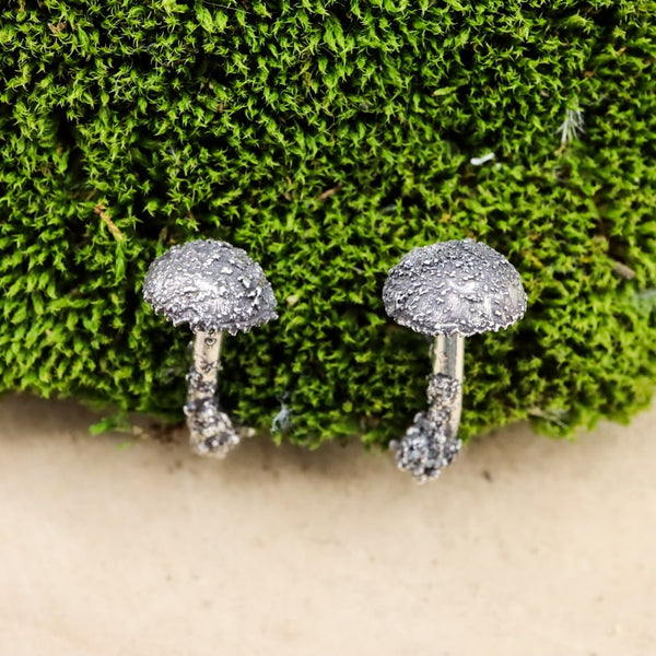 The tops of the silver mushroom earrings. They look realistic with the pattern on the tops. The earrings are shown on a piece of dark green moss. 