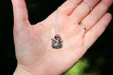 A hand is shown holding the watermelon tourmaline and mushroom forest necklace in the sunlight. 