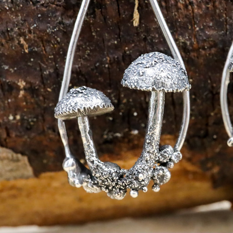 A close up photo of one of the mushroom earrings. There are two small mushrooms sitting inside the hoop with tiny silver ball details that look like soil below them.