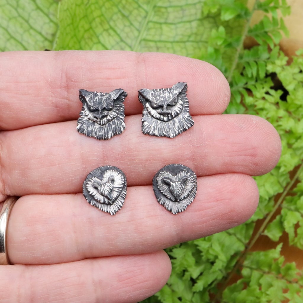A hand is shown holding the barn owl and great horned owl stud earrings for size reference. 