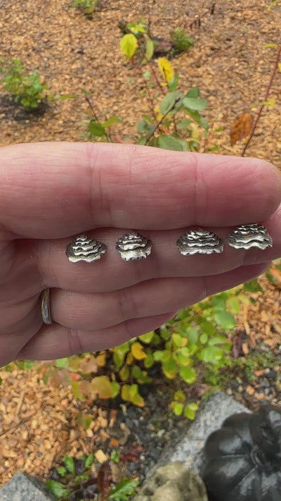 A video showing 4 handmade sterling silver turkey tail mushroom stud earrings being held in a hand showing their texture. 