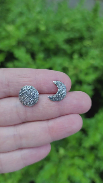 A video is showing a hand holding the mismatched moon earring studs. 