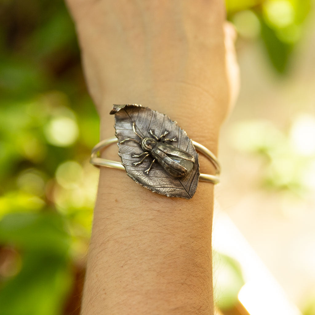 Bracelet with beech leaf and firefly insect design worn on wrist against a natural background